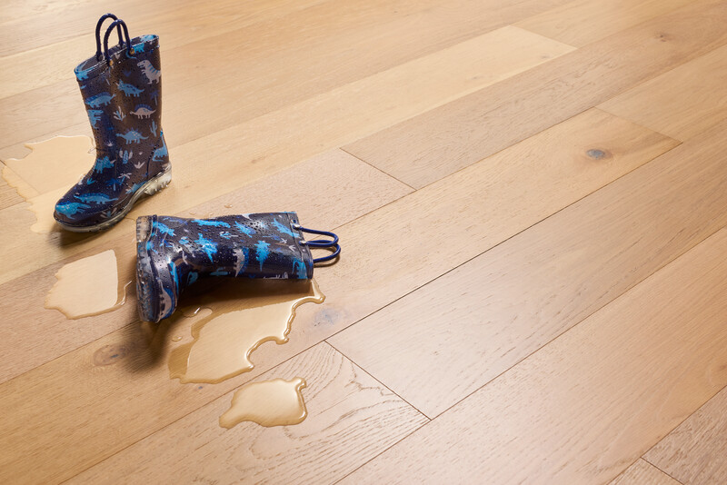 Pair of children's boots with one laying over and a puddle next to it to show waterproof hardwood flooring